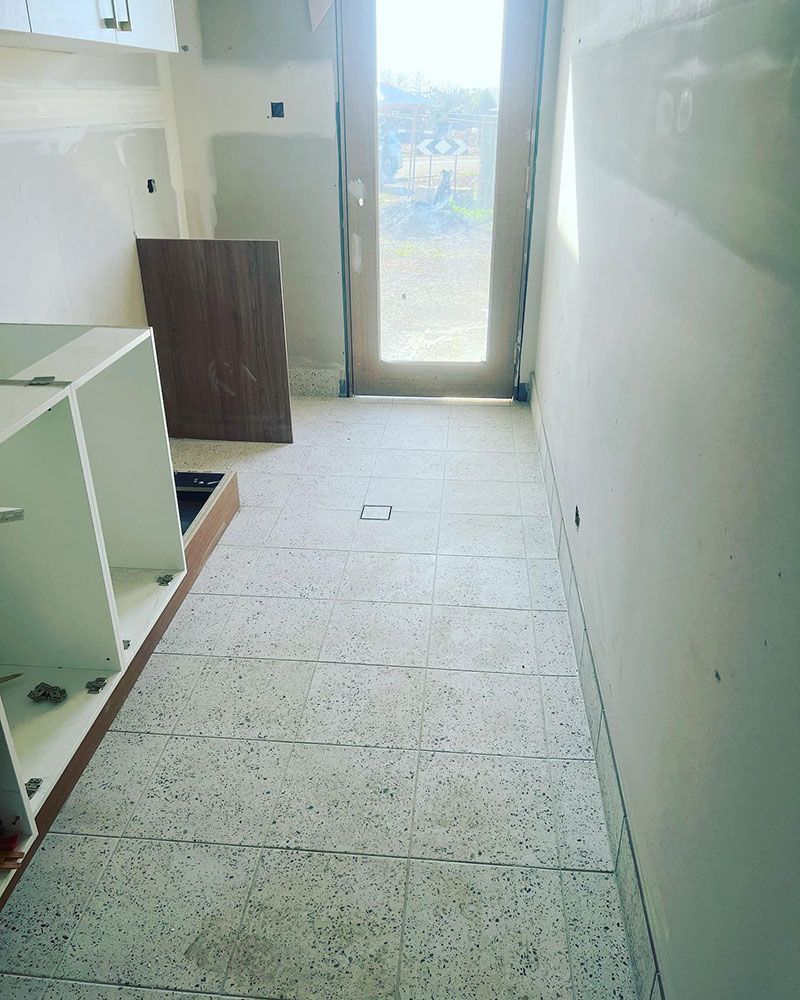 A Kitchen Under Construction With a Tiled Floor and a Door — S & S Tiling and Rendering in Dubbo, NSW
