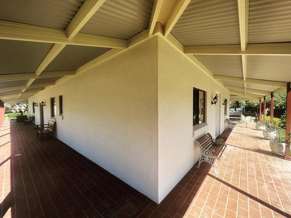 A White Building With a Covered Walkway and a Bench — S & S Tiling and Rendering in Cobar, NSW