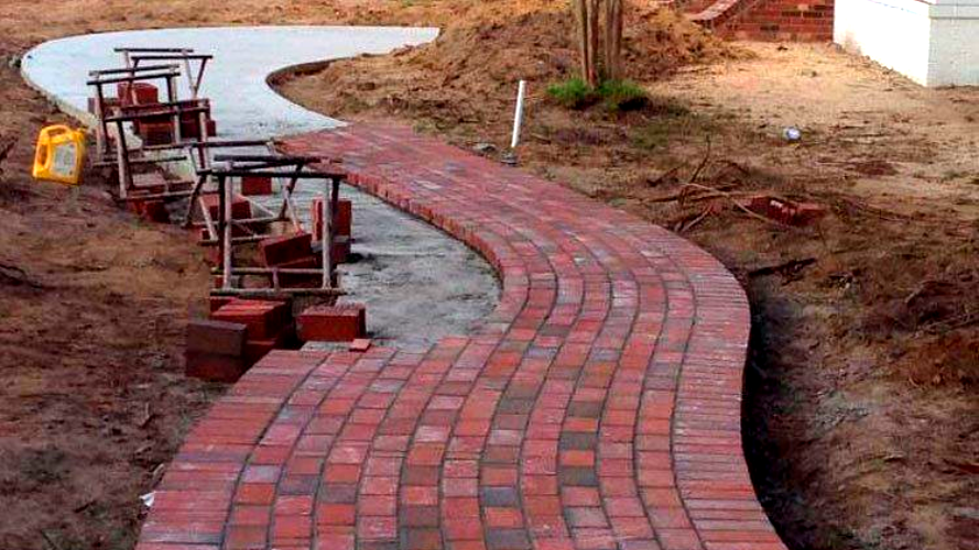 Red brick path under construction, curving through a dirt yard in Wilmington, NC.