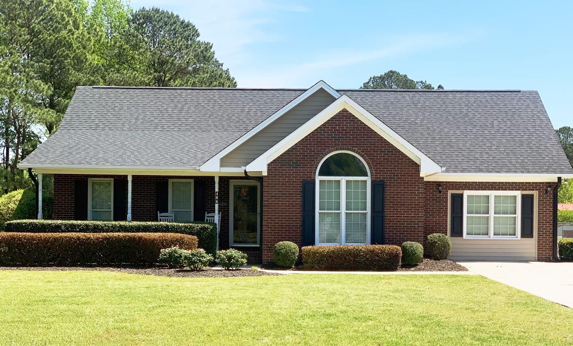 Brick ranch-style house with dark shutters, front porch, and manicured lawn under a blue sky in Wilmington, NC.