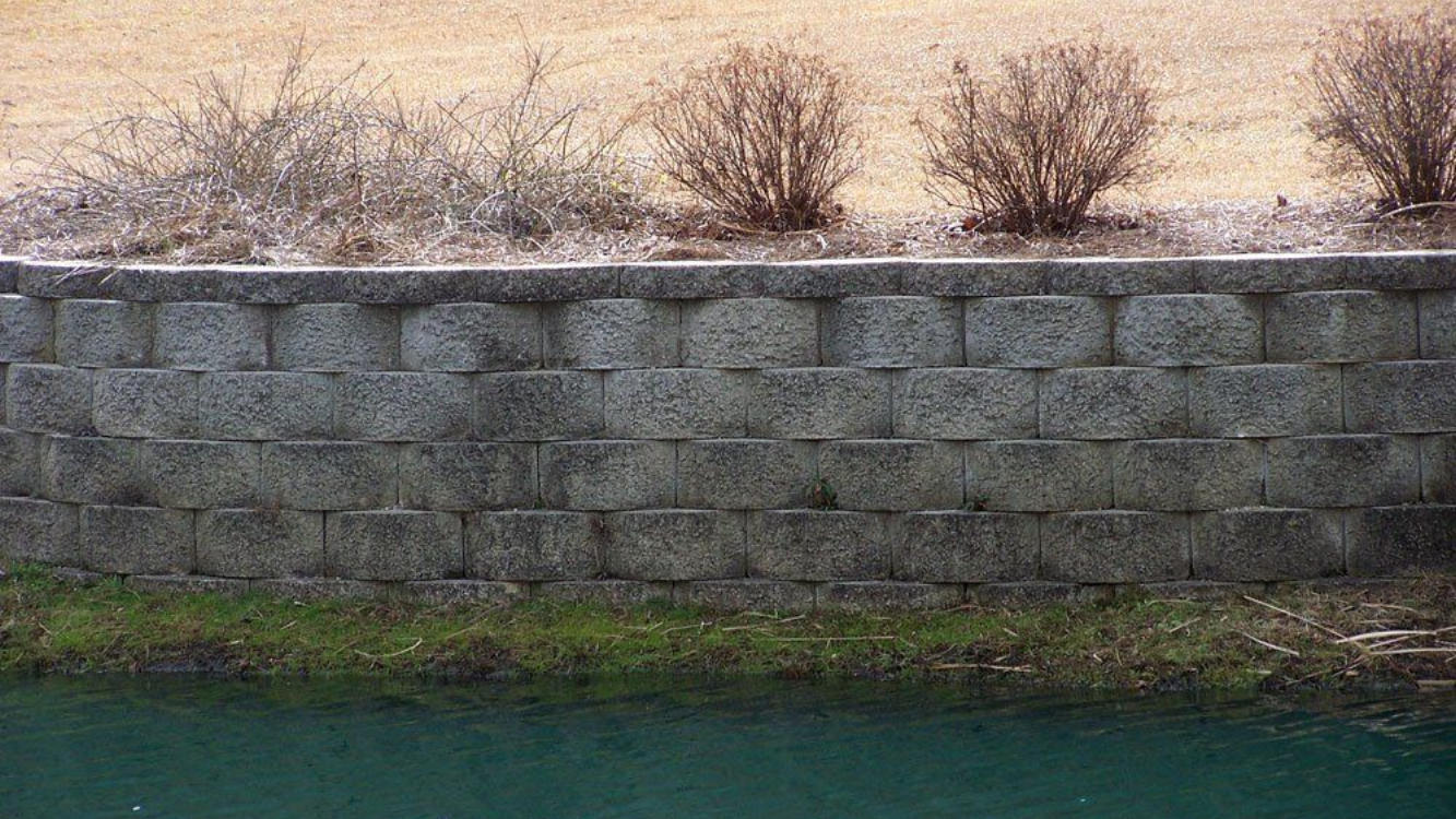 Stone retaining wall with shrubs on top, near water in Wilmington, NC.