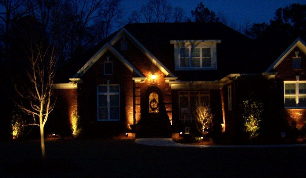 Night view of a house with outdoor lighting illuminating the brick facade, door, and landscaping in Wilmington, NC.