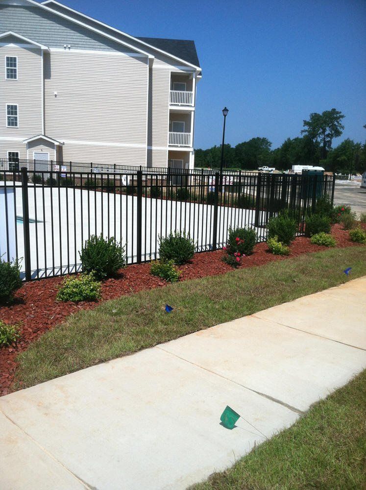 A fence surrounds a swimming pool with a building in the background