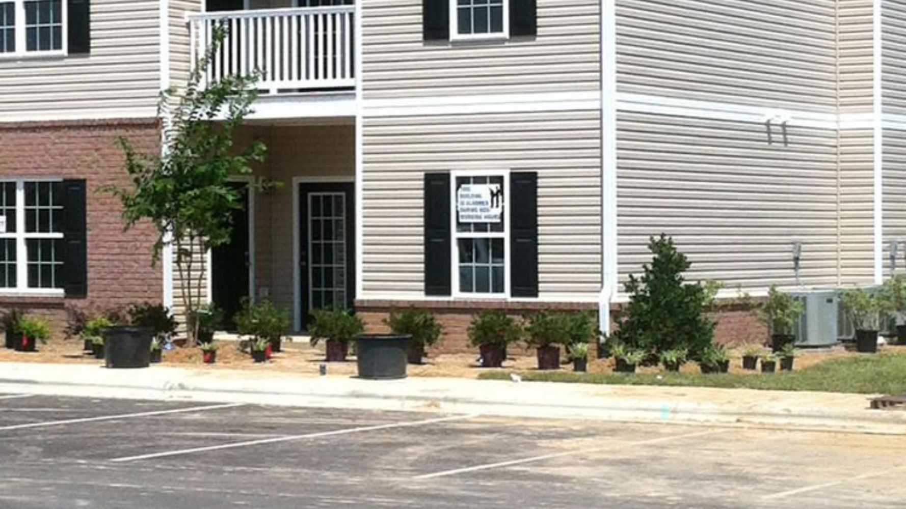 Apartment building exterior with beige siding, black shutters, brick accents, and potted plants in front in Southern Pines, NC