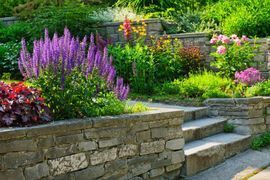 A stone wall surrounds a garden filled with lots of flowers and plants.