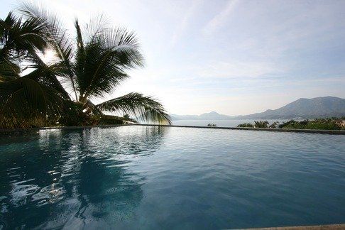 a swimming pool with palm trees and mountains in the background