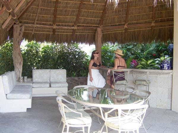 two women sit at a table under a thatched roof