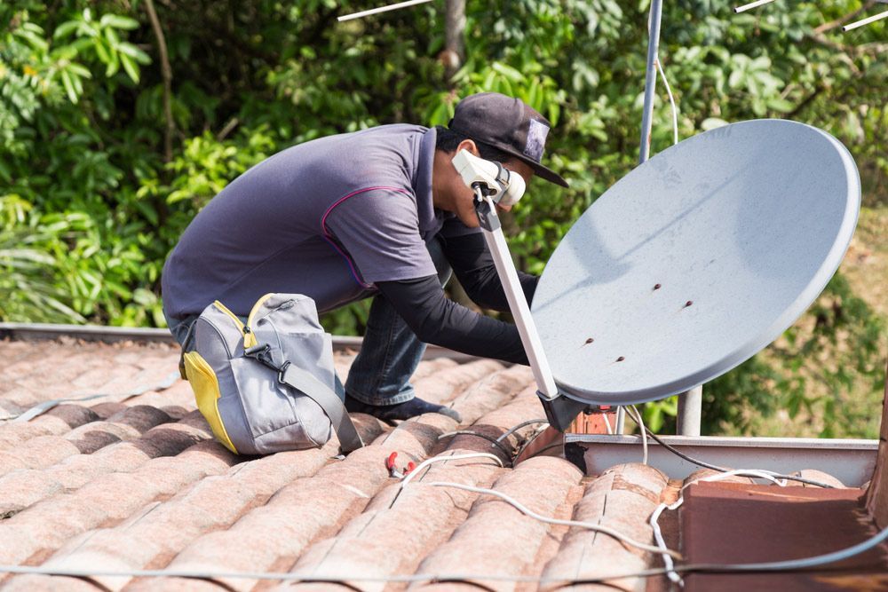 A Man Is Installing a Satellite Dish on The Roof of A House — T.N. Locke Communications In Kirwan, QLD