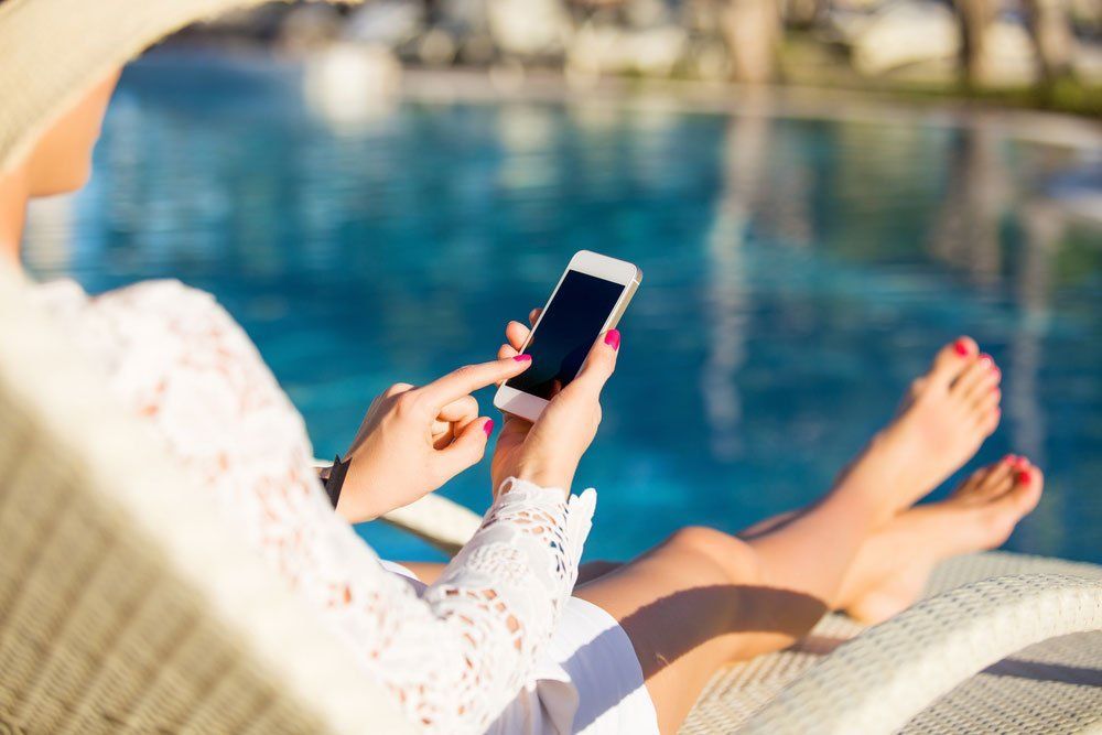 A Woman Is Sitting on A Lounge Chair by A Pool Using a Cell Phone — T.N. Locke Communications In Kirwan, QLD