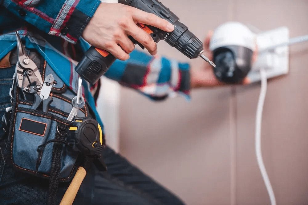 A Man Is Installing a Security Camera with A Drill — T.N. Locke Communications In Kirwan, QLD