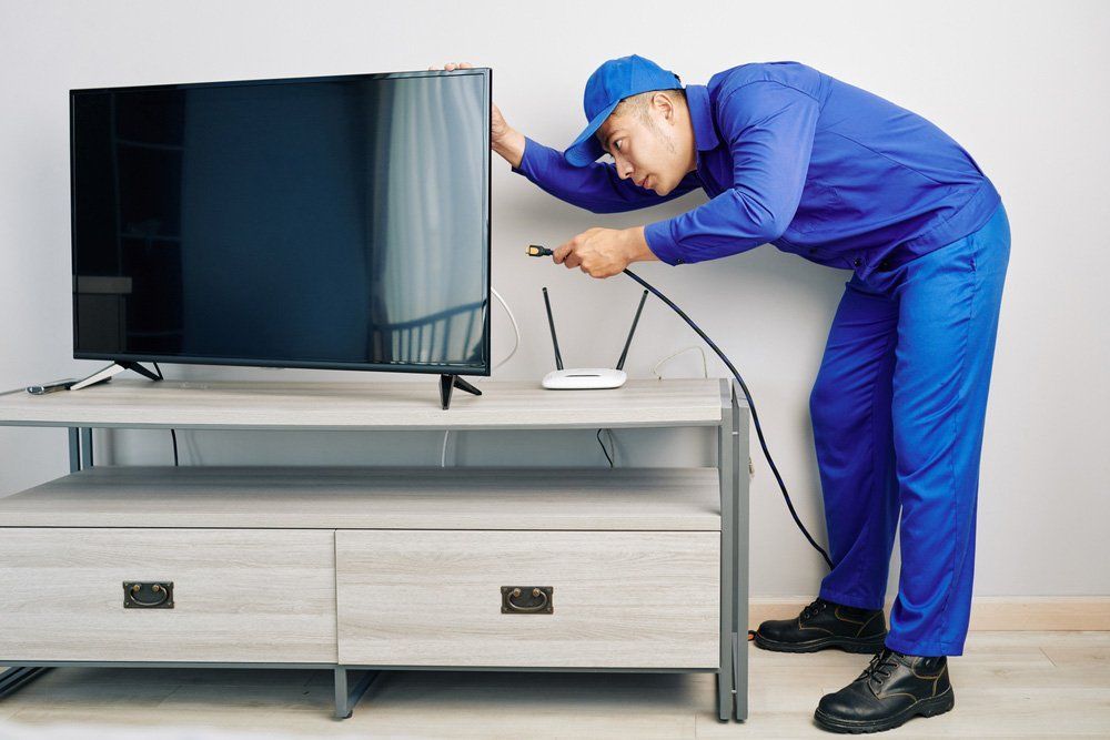 A Man is Fixing a Flat Screen Tv on a Stand — T.N. Locke Communications In Burdekin, QLD