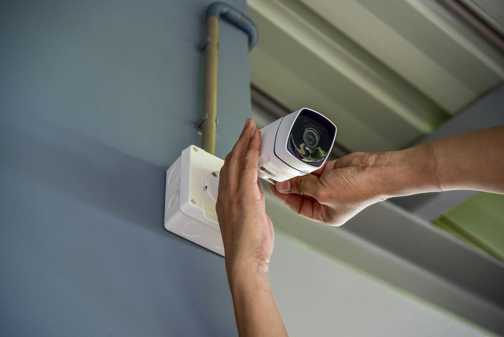 A Person Is Installing a Security Camera on A Wall — T.N. Locke Communications In Kirwan, QLD