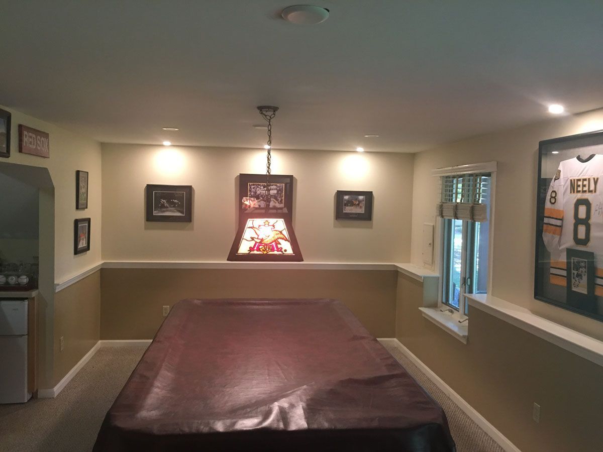 A basement recreation room with a covered pool table, art, recessed lighting, and a hockey jersey.