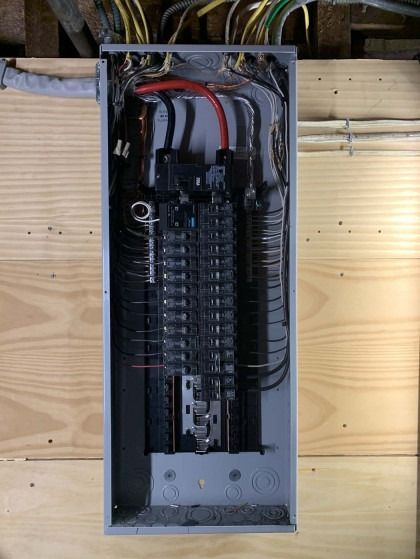 An open electrical panel on a wooden wall; black and silver circuits and wires are visible.