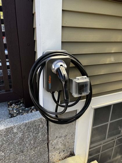 Black EV charger mounted on a house wall, with cable coiled around it.