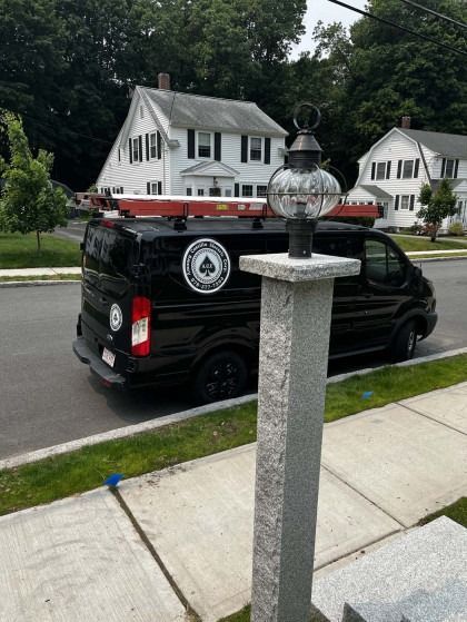 Black van parked on street in front of a white house. Lamp post in foreground.