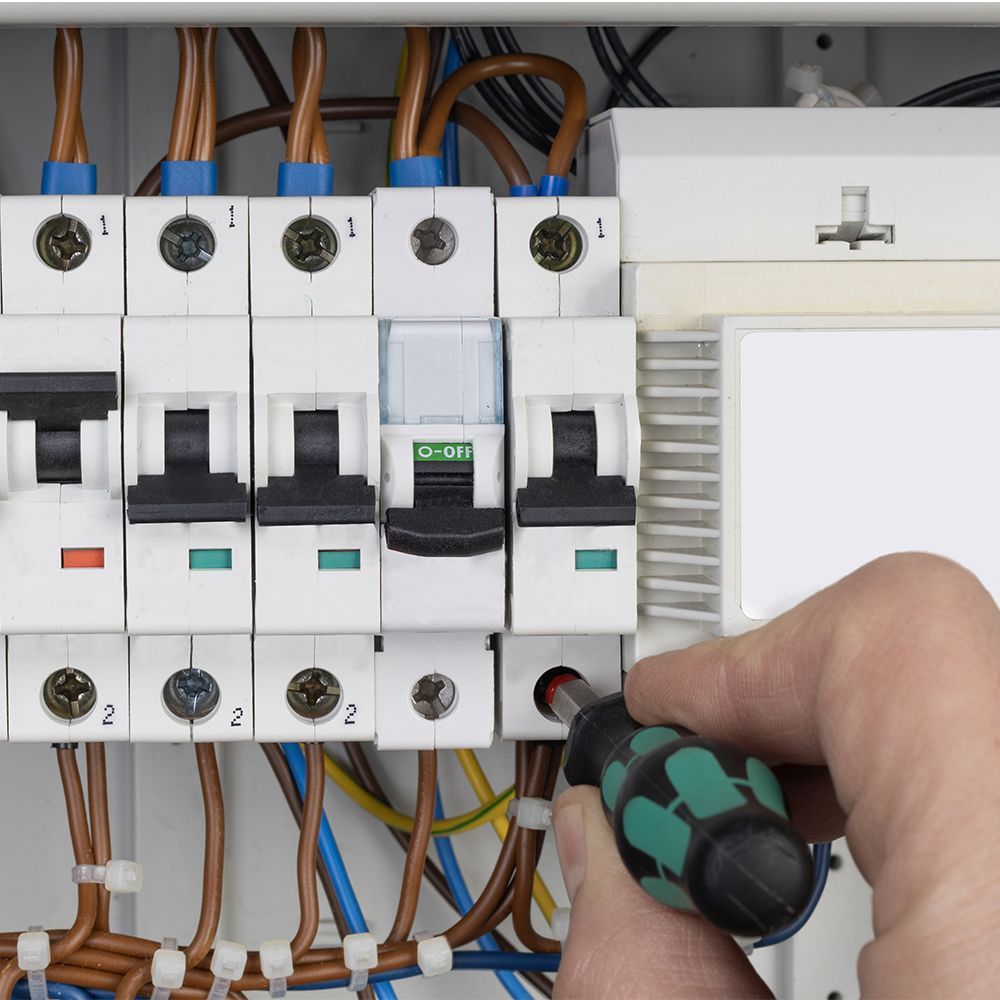 Hand using screwdriver on a circuit breaker panel; wires visible.