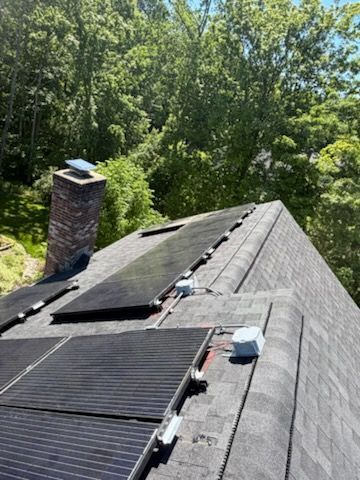 Roof with solar panels and a chimney, surrounded by trees and greenery.