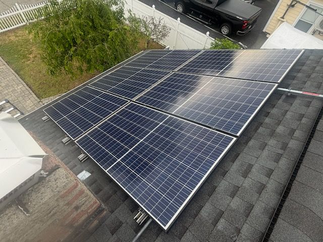 Solar panels installed on a rooftop beside gray shingles and a tree-lined street.