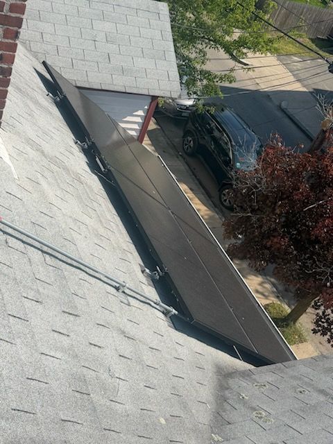 Roof shingles beside a driveway with a parked black car and a tree below.