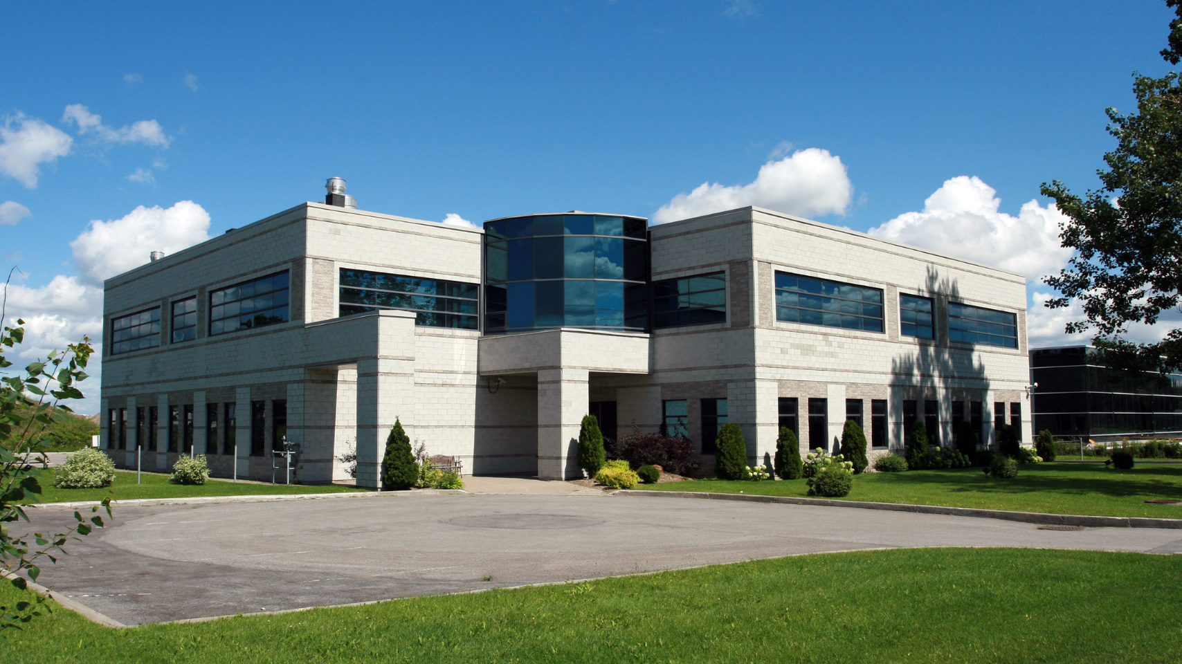 Modern office building with dark glass accents, surrounded by green lawn under a blue sky.