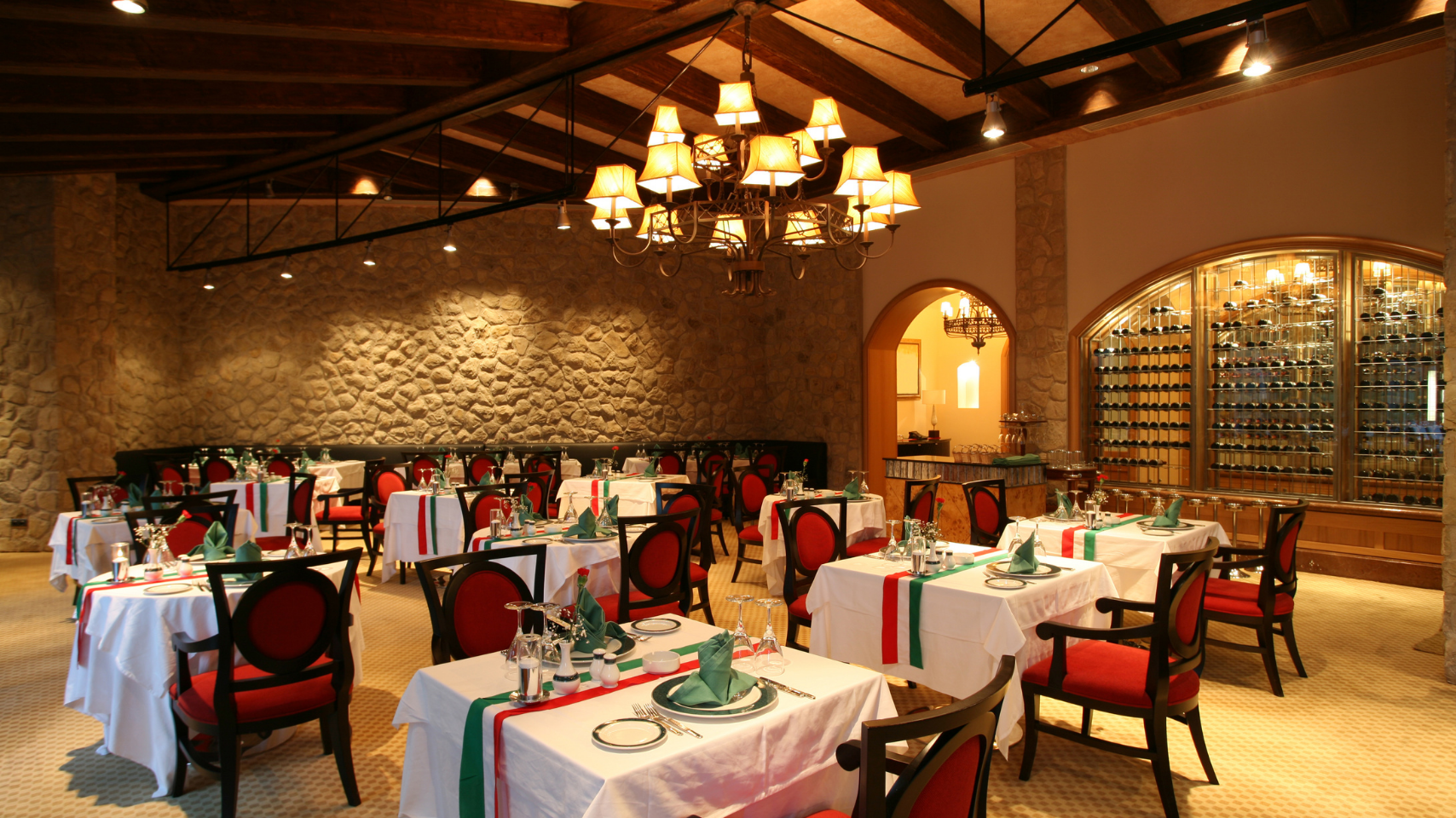 Elegant restaurant dining room with white-clothed tables, red chairs, brick walls, and warm chandeliers