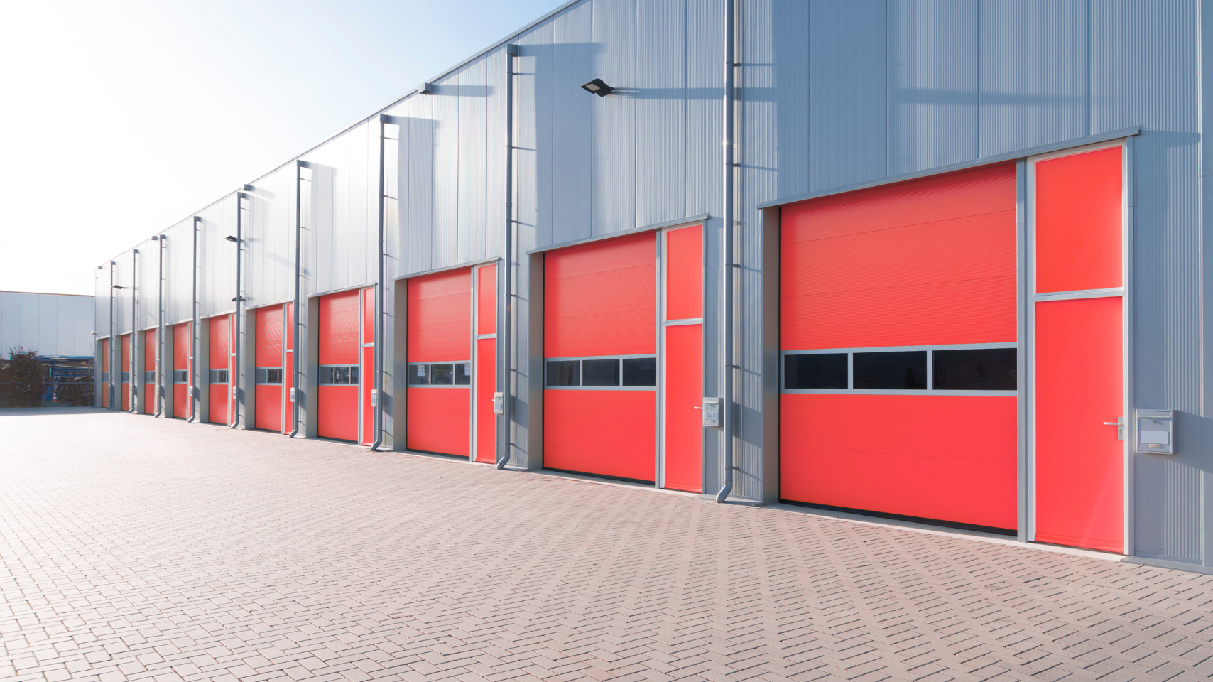 Row of red industrial warehouse doors along a gray metal building in bright daylight