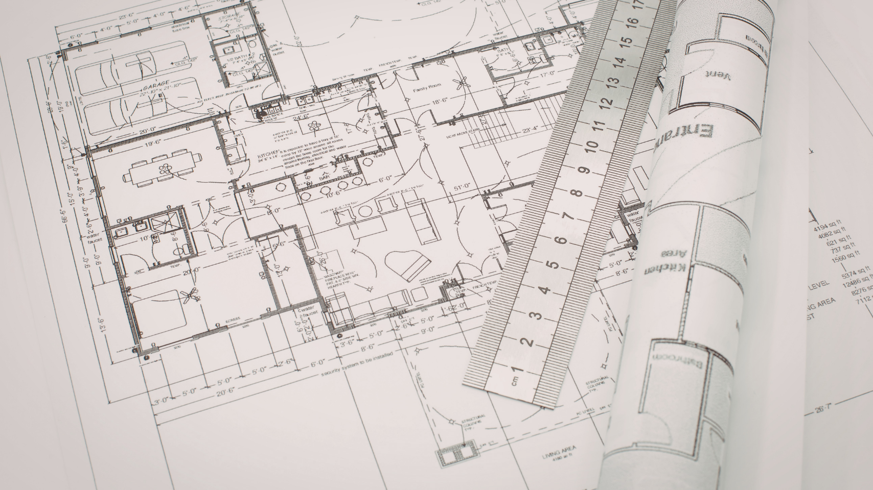 Architectural floor plans with a ruler and rolled blueprint on a desk.