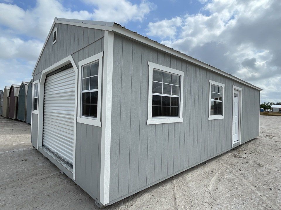 Superior Outdoor Centers Garage Portable A gray garage with white trim and windows is sitting on top of a dirt field.