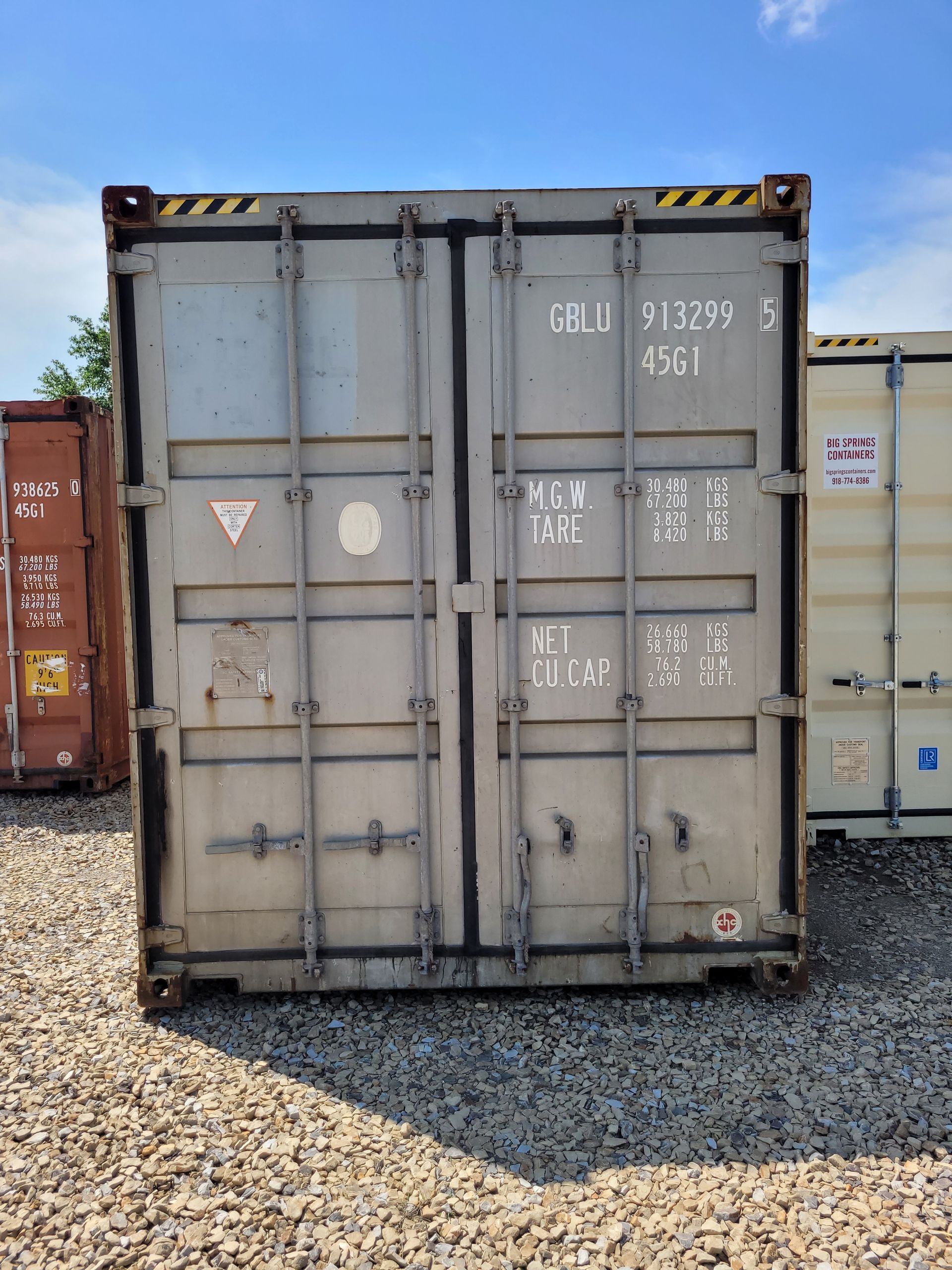 A shipping container is sitting in a gravel lot.