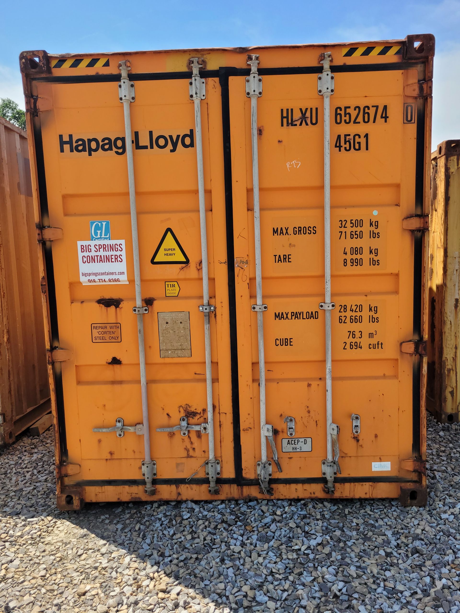 An orange hapag lloyd shipping container is sitting on gravel