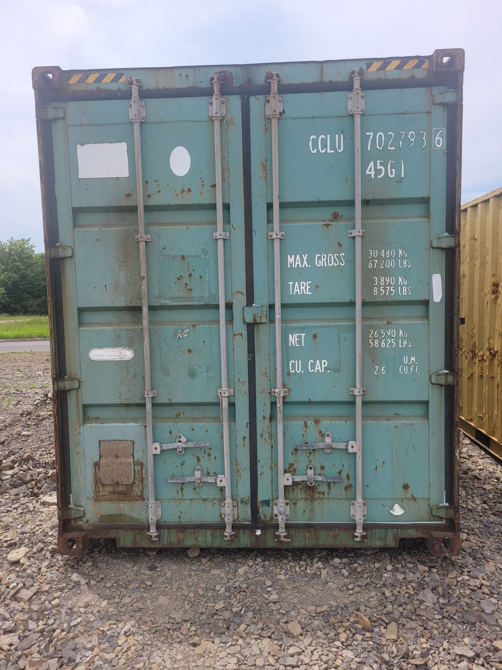 A blue shipping container is sitting in a gravel lot.