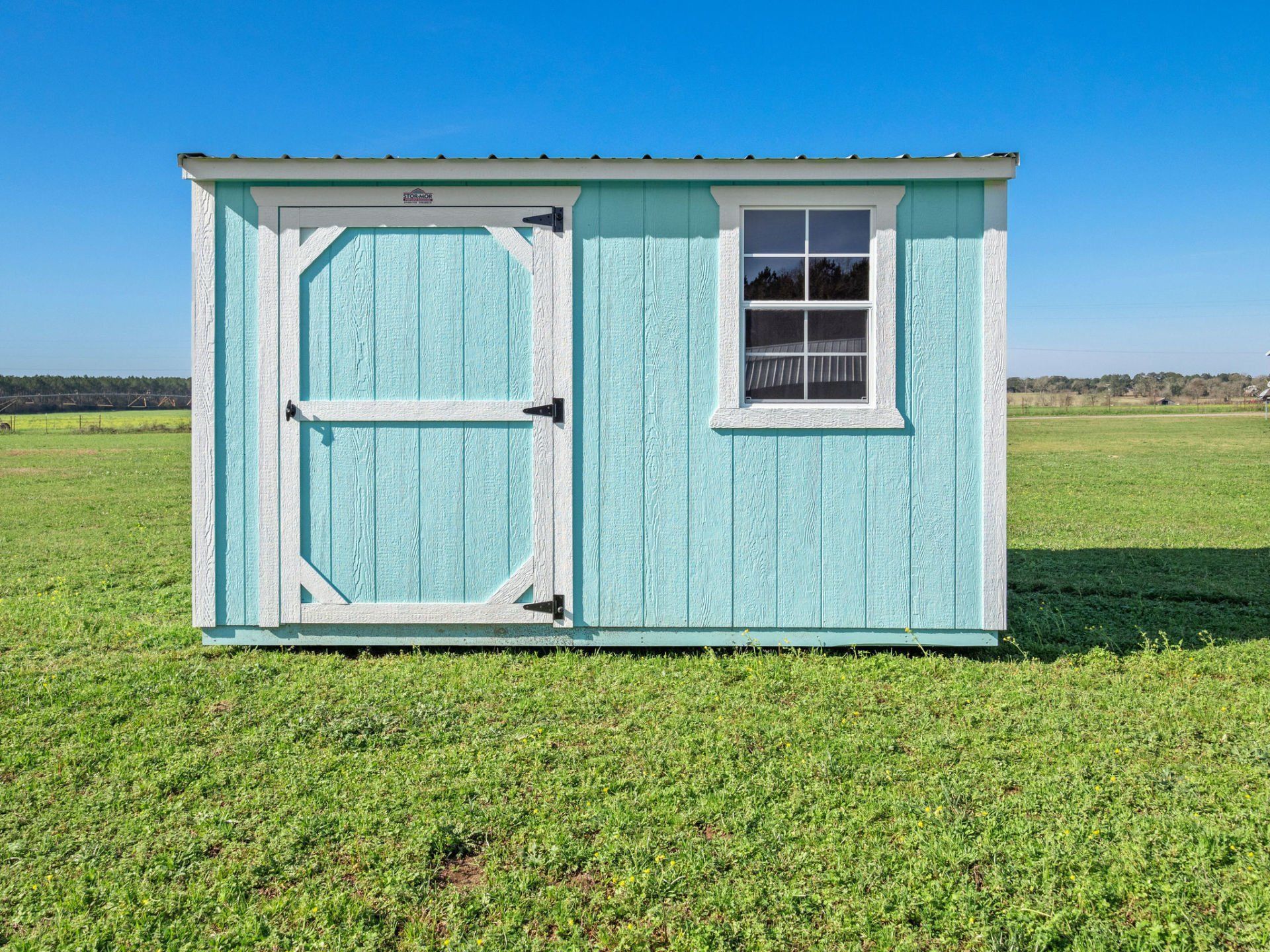 Superior Outdoor Centers garden shed A blue and white shed with a window is sitting in the middle of a grassy field.
