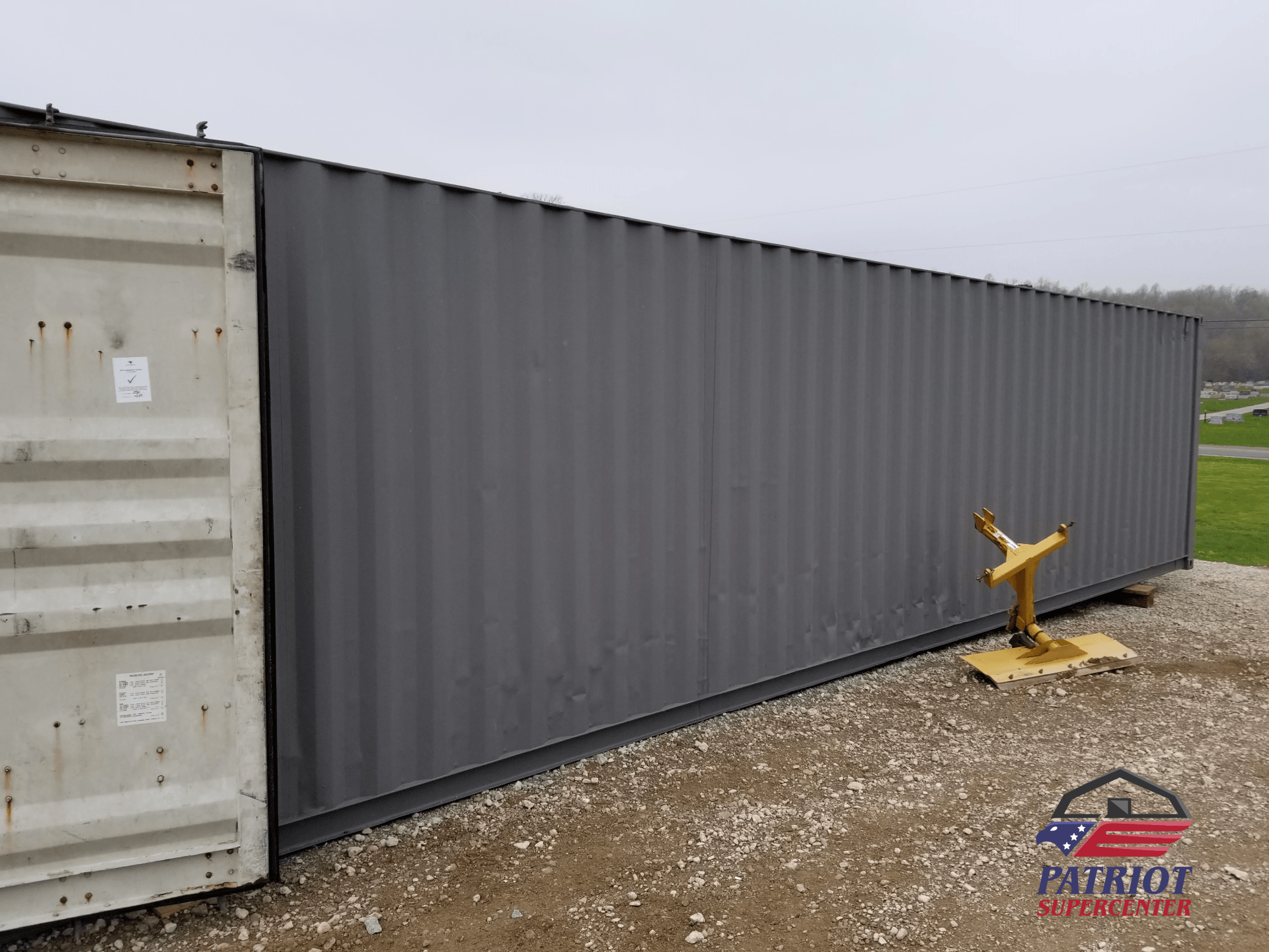 A gray shipping container is sitting next to a white shipping container.