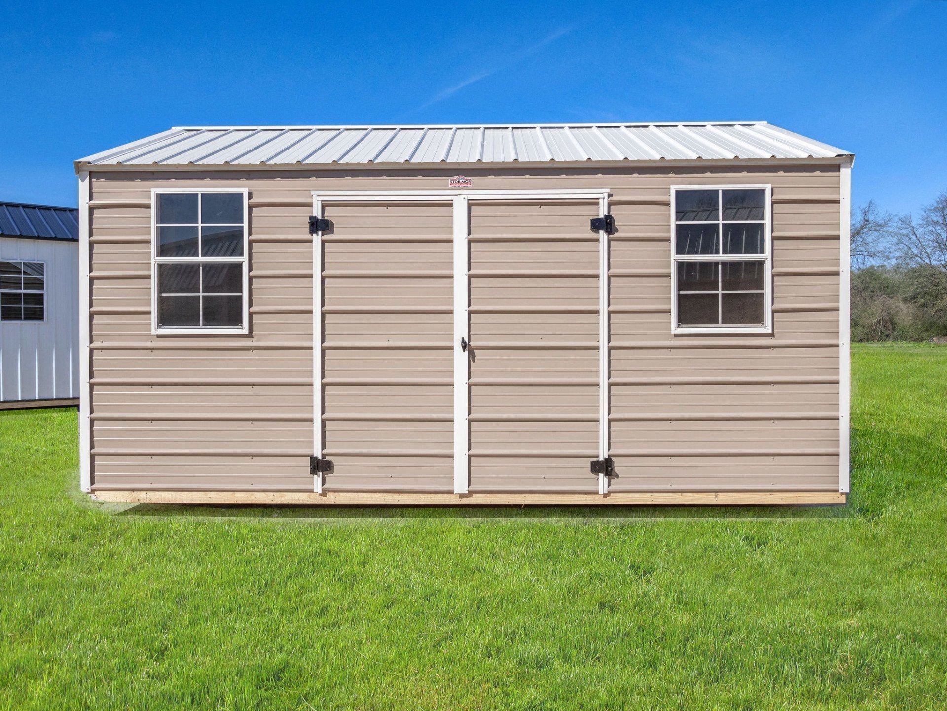 Superior Outdoor Centers  metal side utility shed A metal shed with two windows is sitting in the middle of a grassy field.
