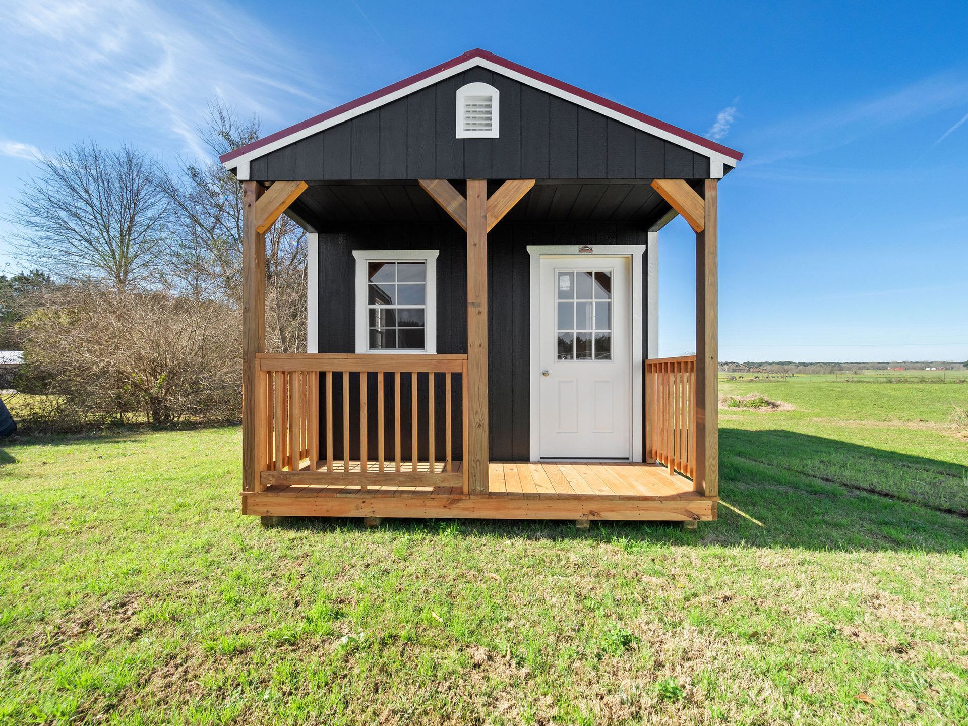 Superior Outdoor Centers  cabin A small black house with a porch in the middle of a grassy field.