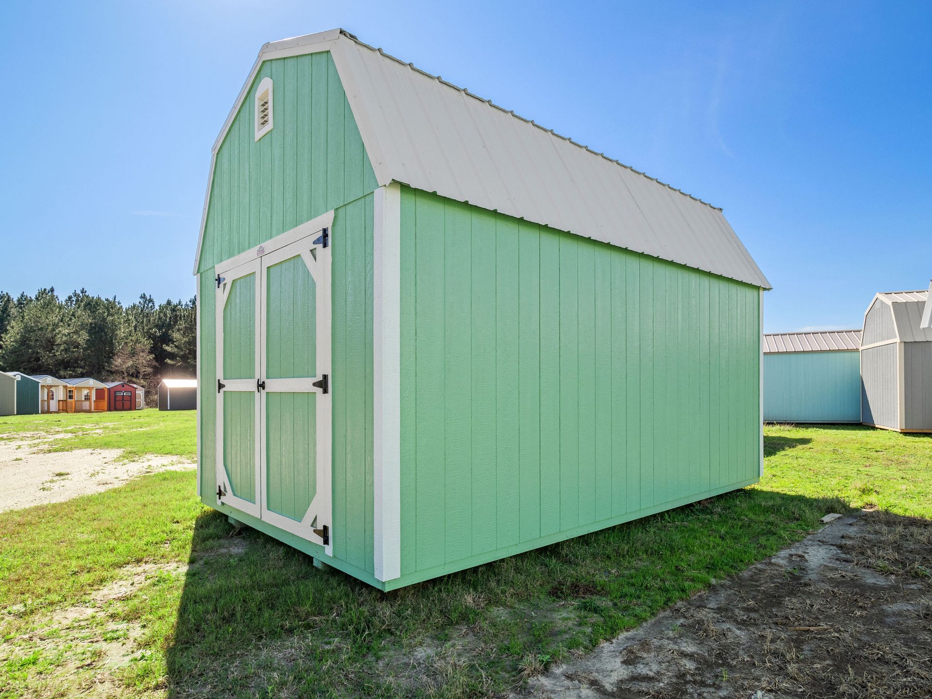 Superior Outdoor Centers lofted barn A green and white barn shed is sitting in the middle of a grassy field.