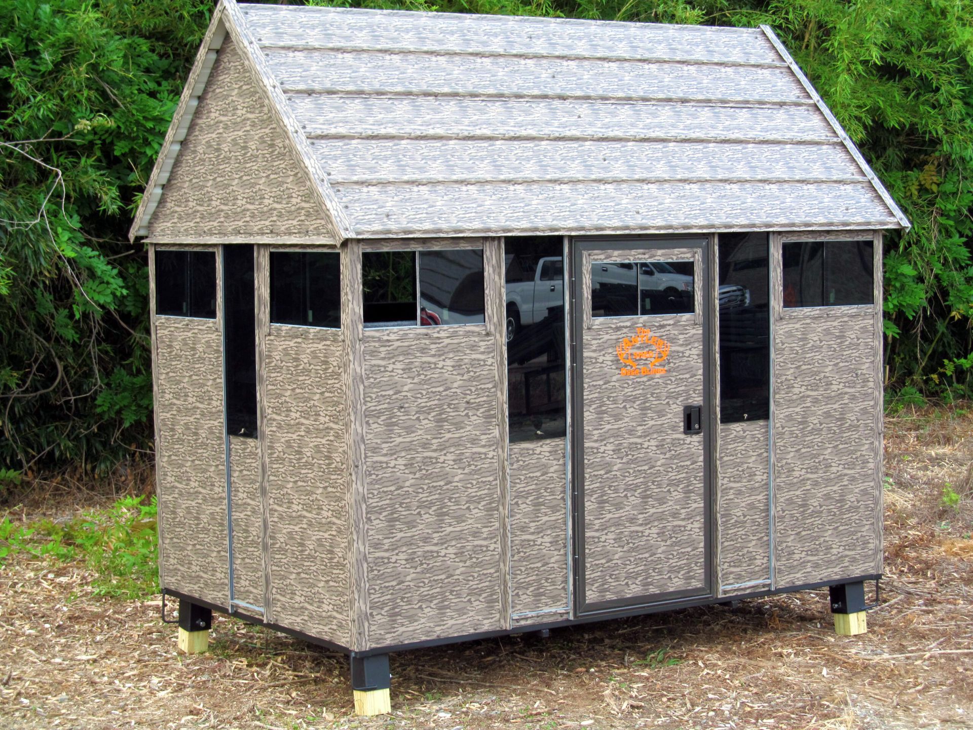 Superior Outdoor Centers Deer Blind A small shed with a roof and a door is sitting in the dirt.
