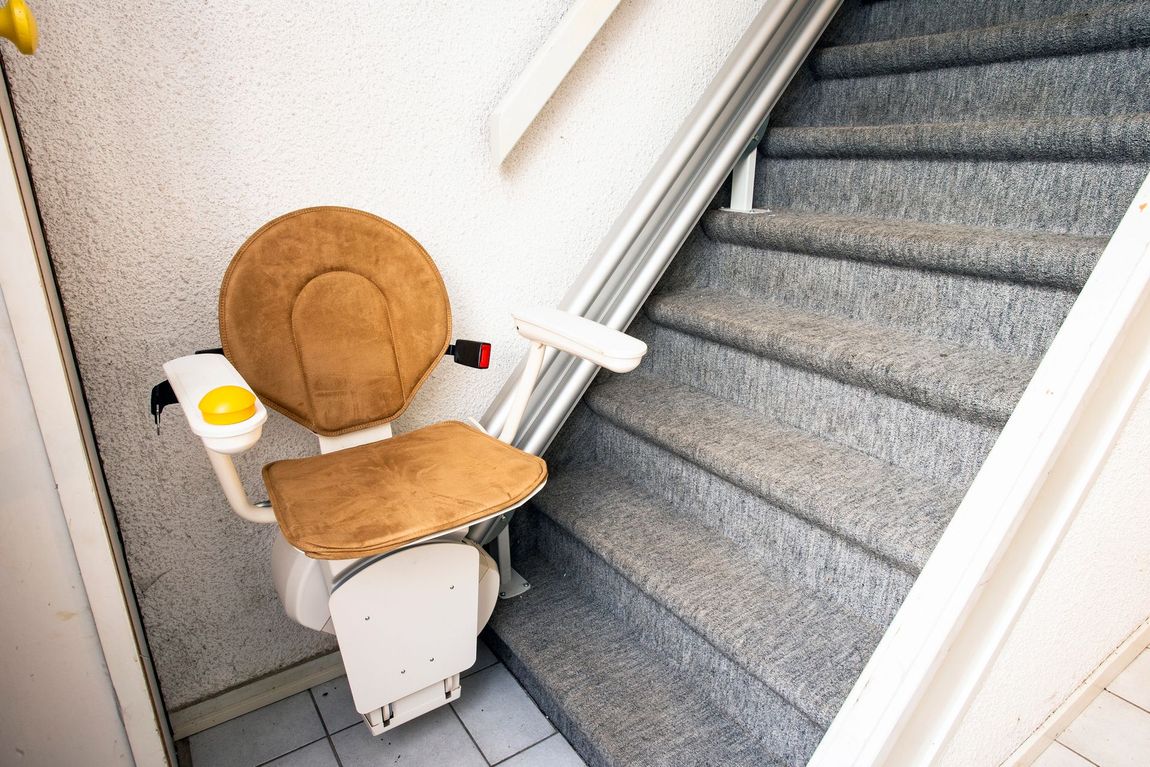 Montascale interno con sedile color beige accanto a una scala rivestita di moquette e corrimano bianco.