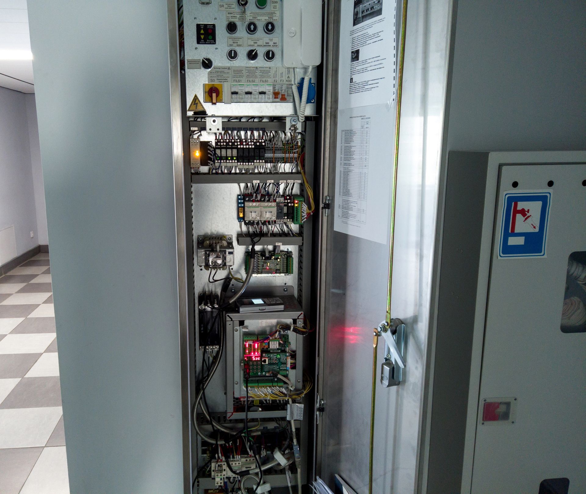 Armadio elettrico aperto con cablaggi, schede elettroniche e spie luminose rosse in un locale di servizio.