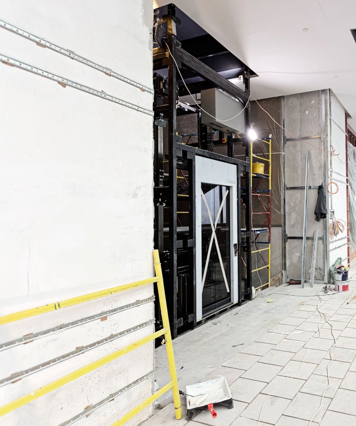 Cantiere edile interno con parete non rifinita, struttura metallica, scala e pavimento piastrellato.