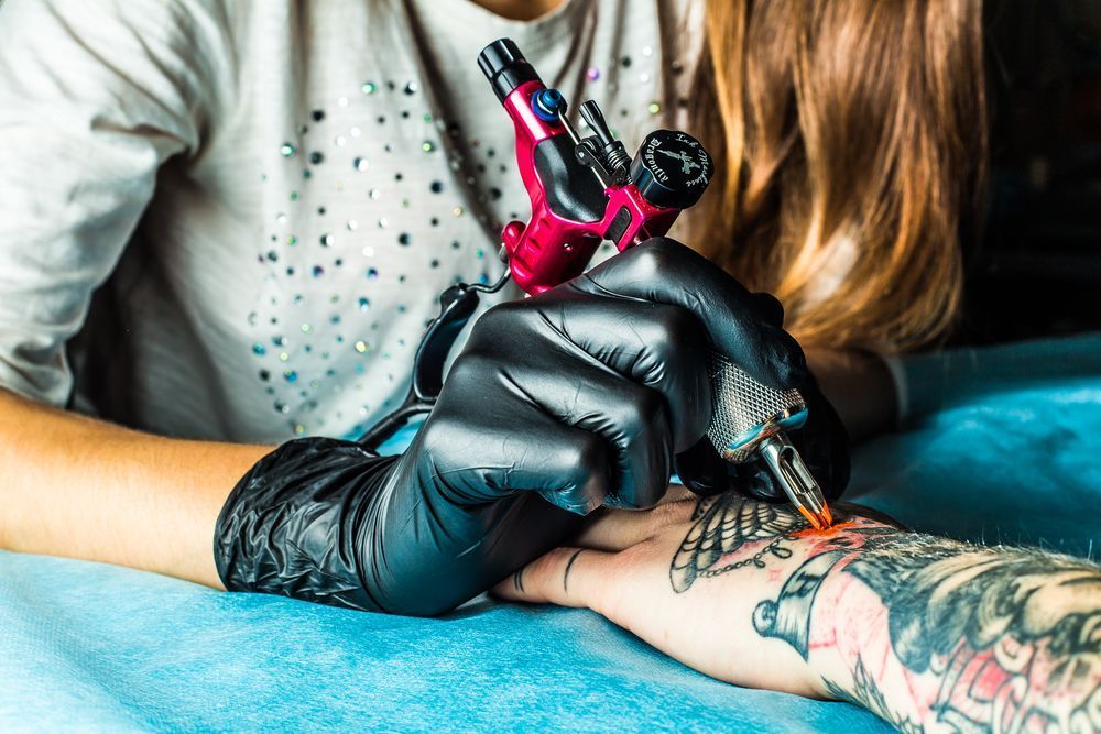 Tattoo Artist With Black Gloves Using Tattoo Machine On A Person's Wrist — Tattoo Inc Studio in Surfers Paradise, QLD