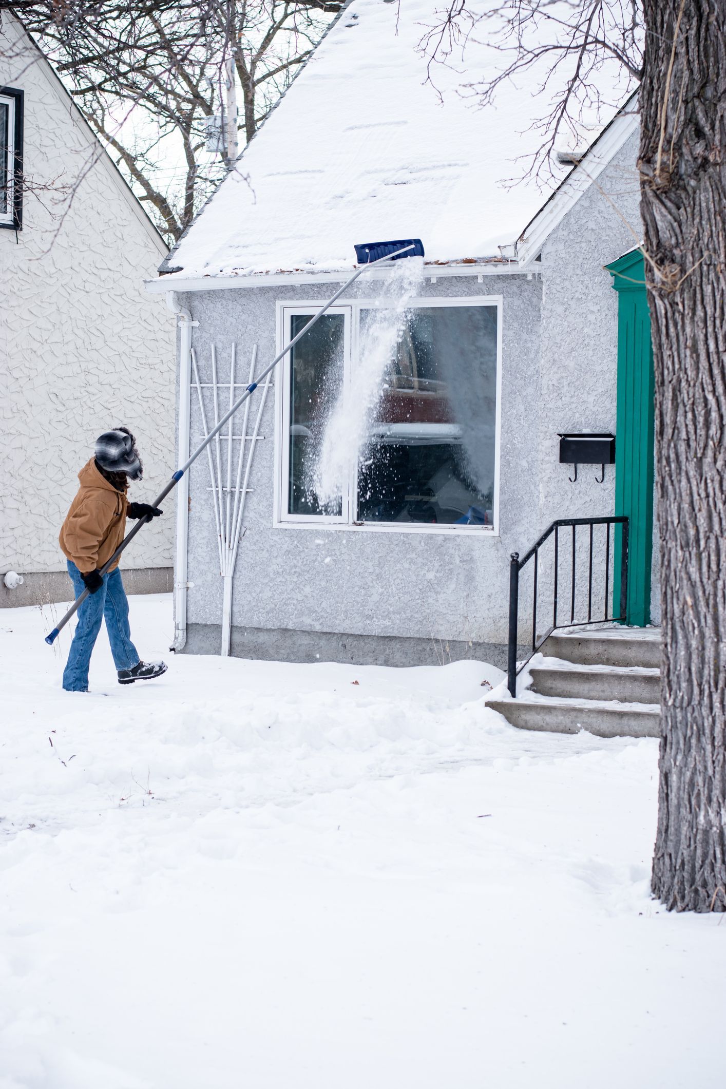 A man is clearing snow from the roof of a house.