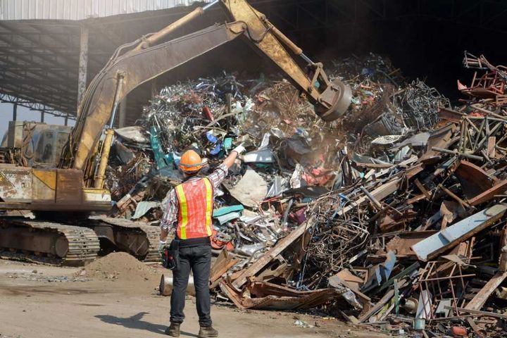 A man is standing in front of a pile of scrap metal.