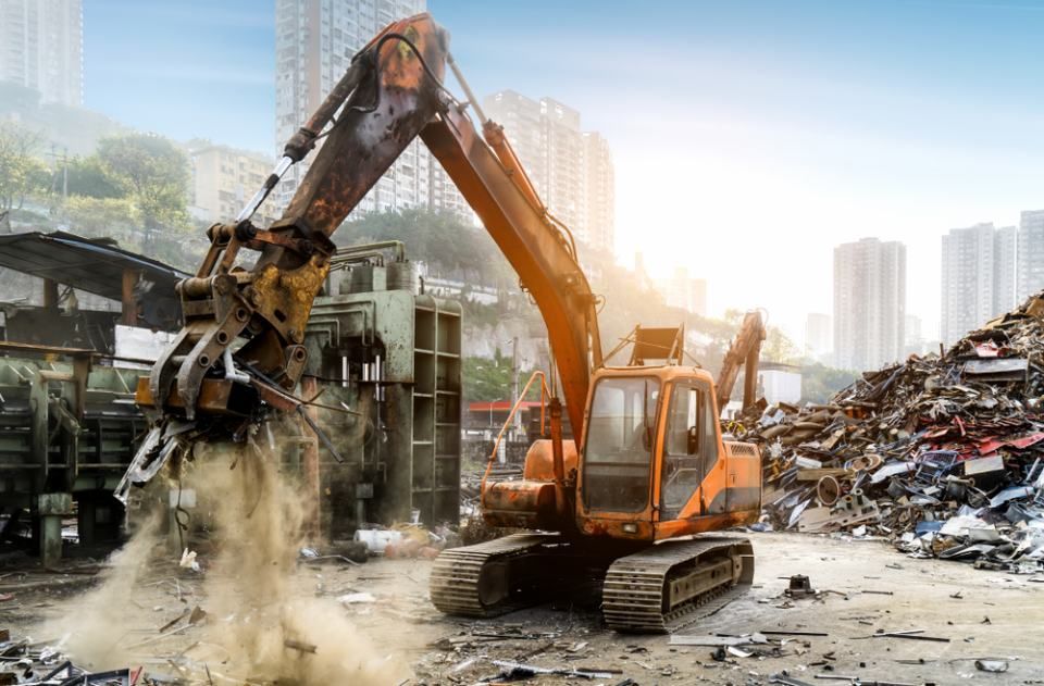 An excavator is loading a pile of scrap metal into a truck.
