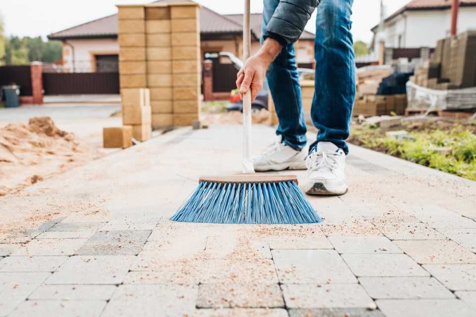 A man is sweeping the sidewalk with a broom.