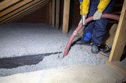 Worker blowing loose insulation into attic with a red hose
