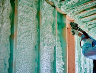 Person spray-foaming insulation into wall studs inside an unfinished building