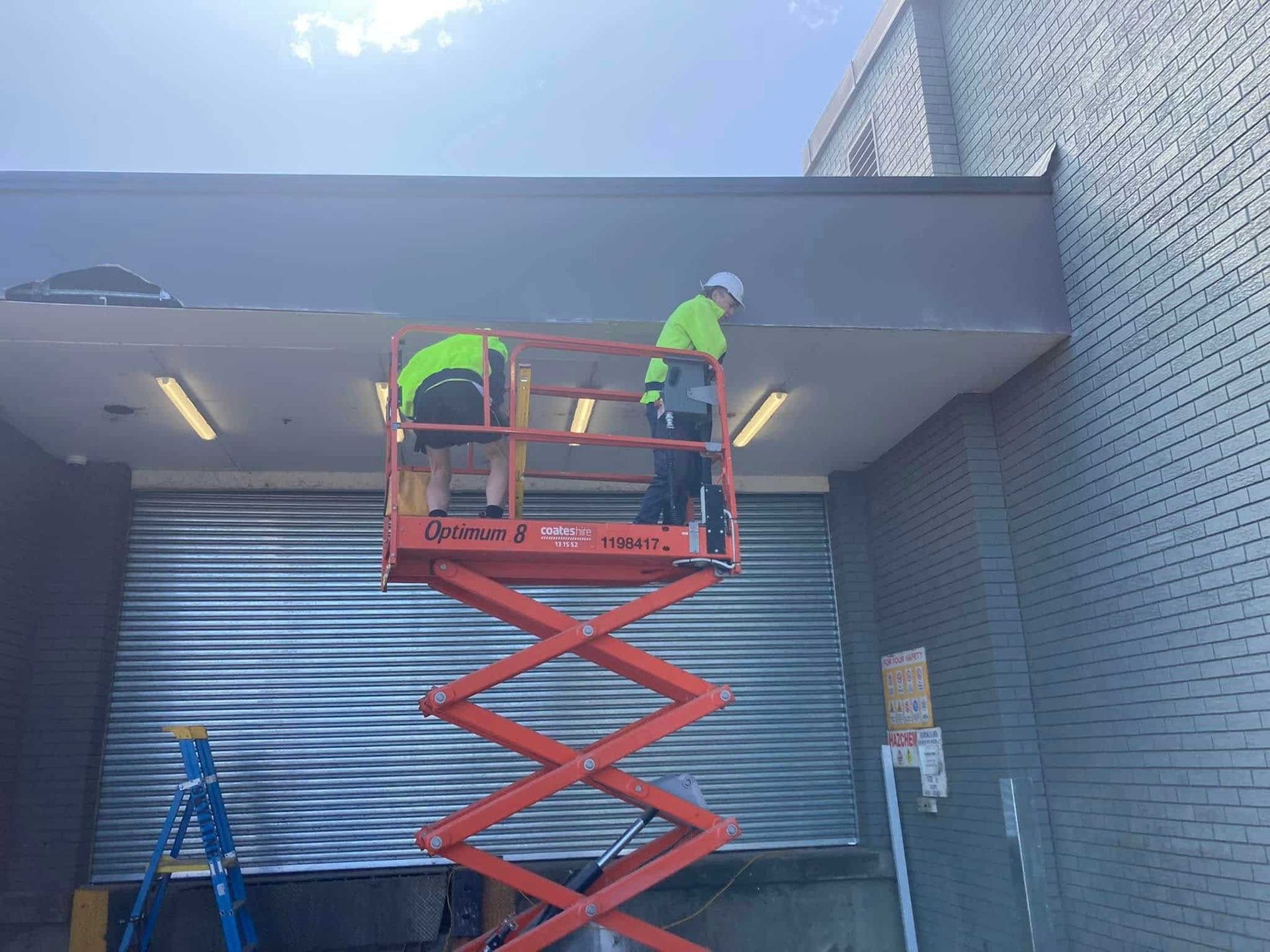 Two Workers on a Red Scissor Lift — SJ Moore Plumbing & Roofing in Wagga Wagga, NSW