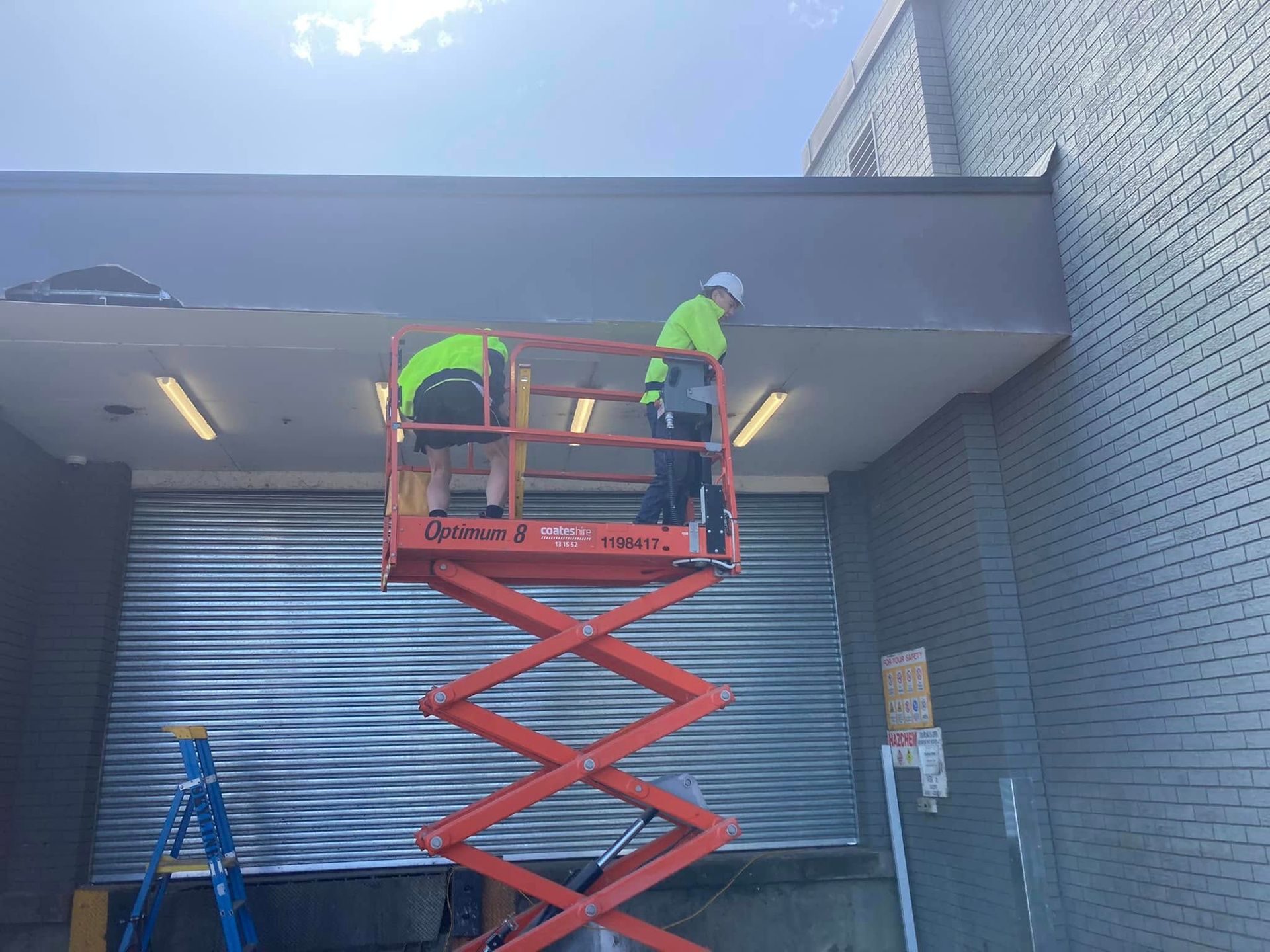 Two Workers on a Red Scissor Lift — SJ Moore Plumbing & Roofing in Wagga Wagga, NSW